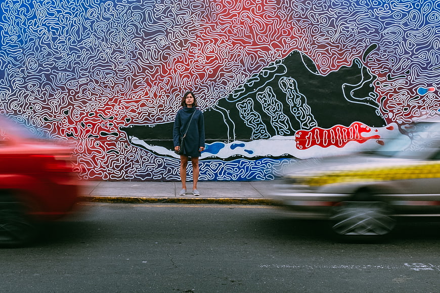 Woman standing before colorful street art mural with blurred traffic