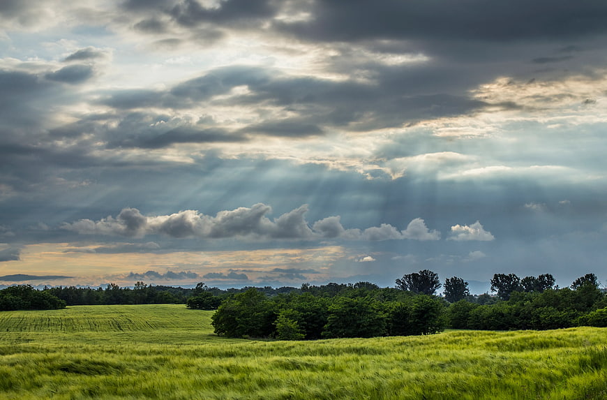 Dramatic Sun Rays Breaking Through Clouds Over Green Fields
