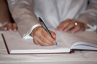 Close-up of groom signing marriage certificate with pen