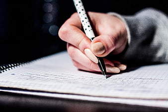 Close-up of hand writing in notebook with pen