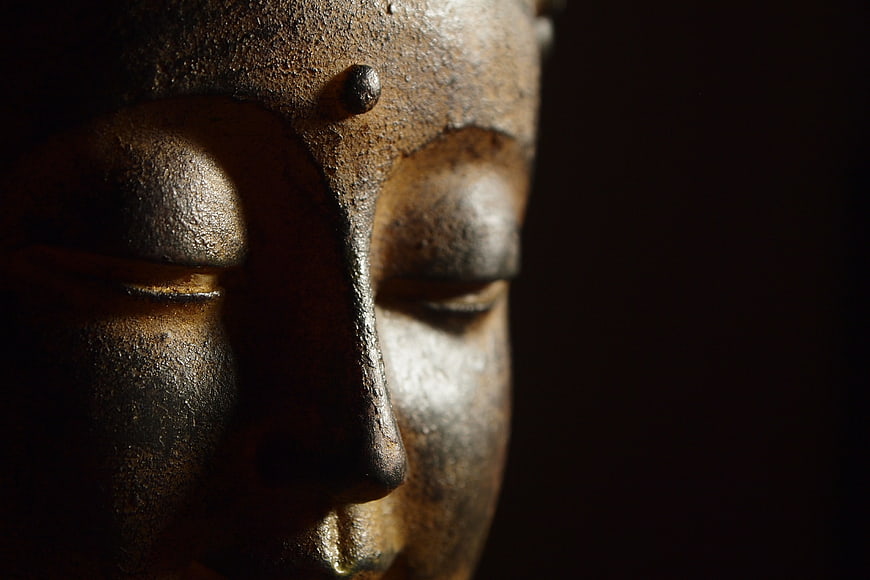 Close-up of bronze Buddha statue face in shadow