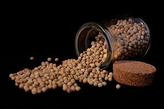 Spilled White Pepper Corns from Glass Jar on Black Background