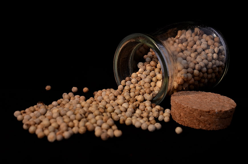 Spilled White Pepper Corns from Glass Jar on Black Background