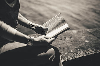 Close-up of hands reading a book by the water