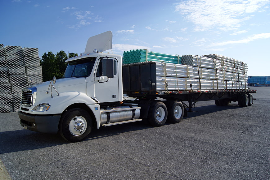 White semi-truck hauling construction pipes on flatbed trailer