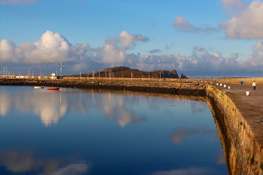 Serene harbor with calm water reflecting clouds and stone breakwater