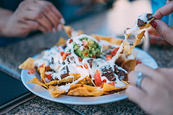 Cheesy Nachos with Guacamole and Sour Cream Being Shared