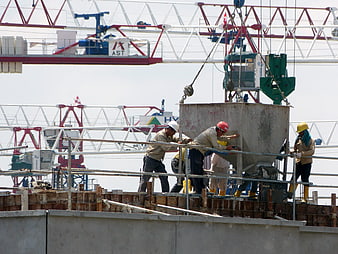 Construction workers guiding concrete hopper on site