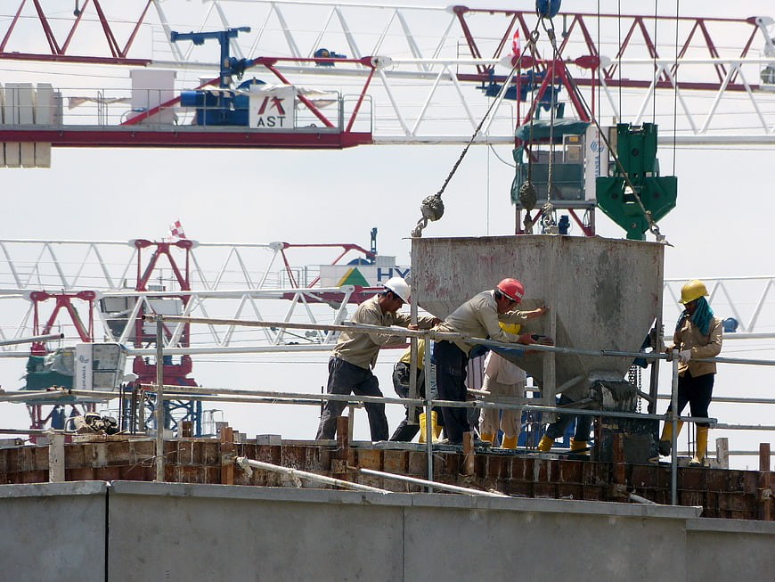 Construction workers guiding concrete hopper on site