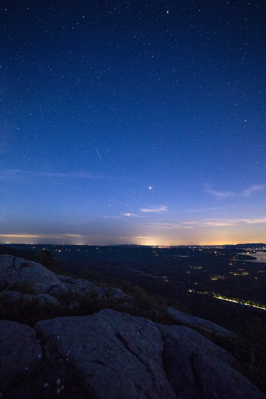 Starry Night Sky Over Rocky Landscape with City Lights