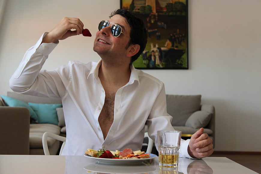 Man in white shirt and sunglasses eating strawberries at a dining table