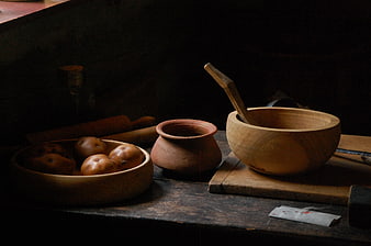 Rustic wooden bowls, clay pot, and potatoes in dark vintage kitchen setting