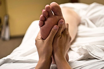 Close-up of hands massaging a foot on a bed