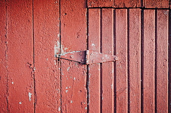 Close-up of weathered red wooden door with metal hinge