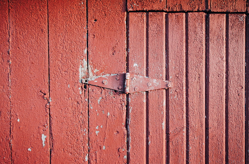 Close-up of weathered red wooden door with metal hinge