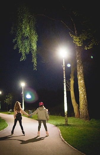 Two Girls Rollerblading at Night Holding Hands in Park