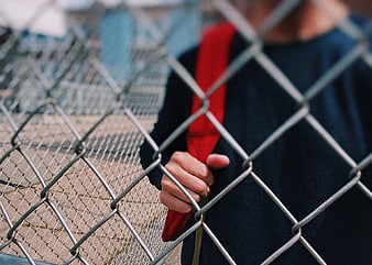 Teenager holding red tie behind chain link fence