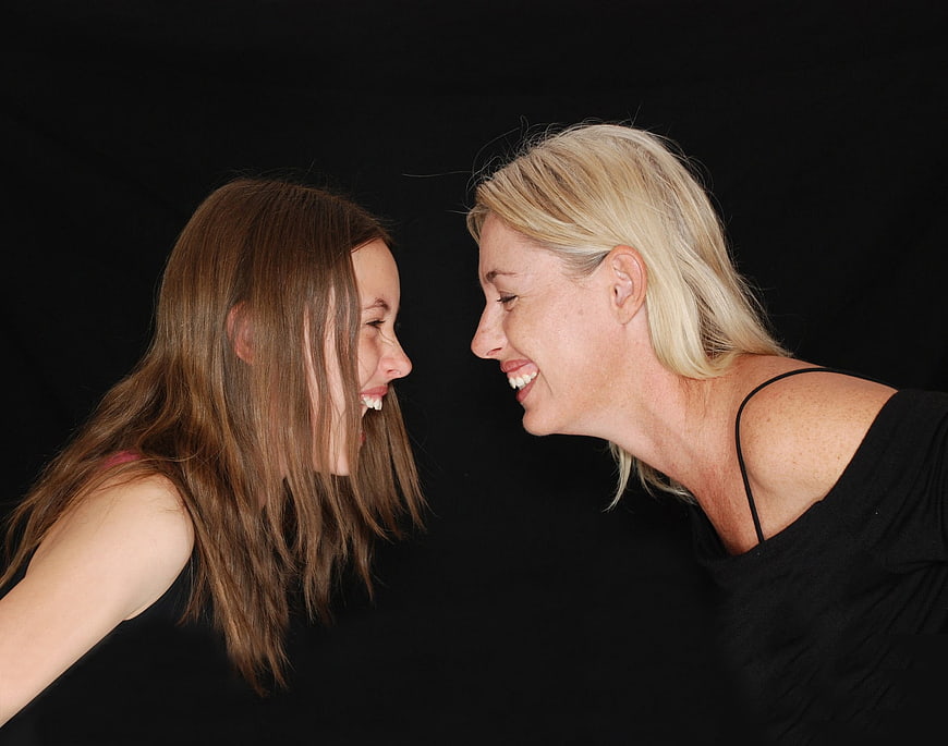Mother and daughter laughing together against black background