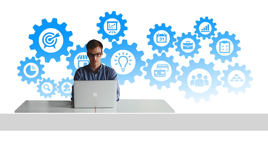Young businessman working on laptop with business gear icons