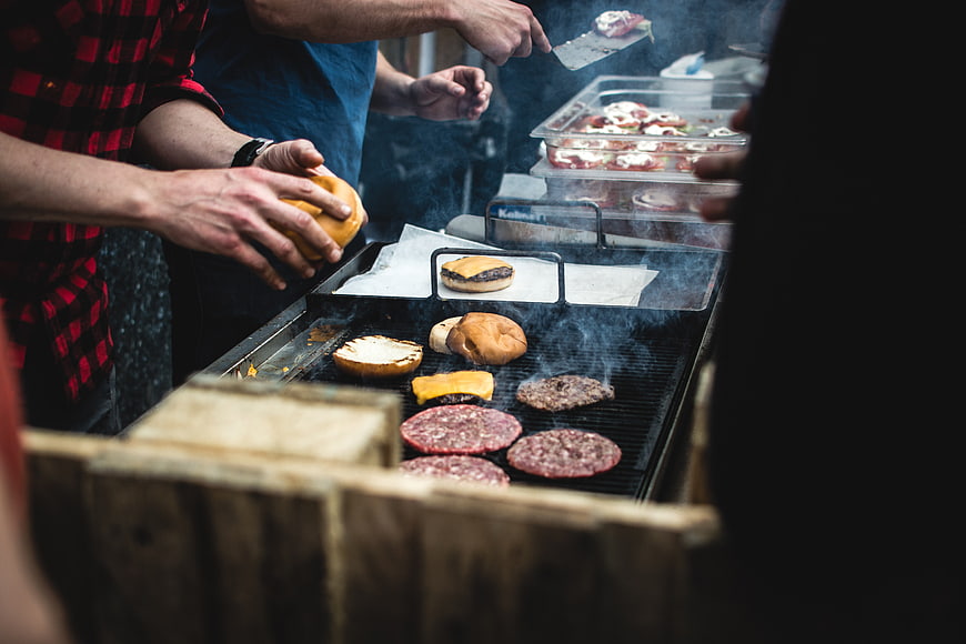 Hands grilling beef burgers and buns on a barbecue grill