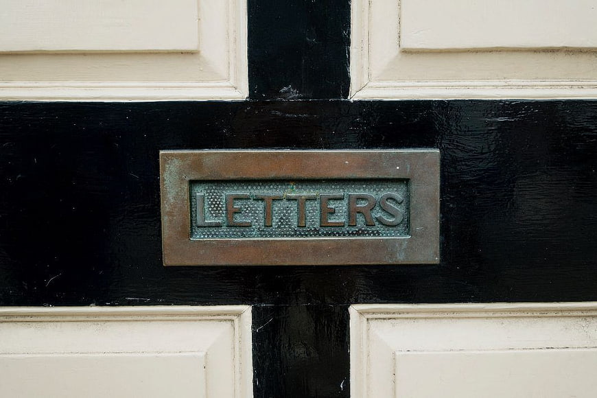 Close-up of vintage brass letterbox on black and white door