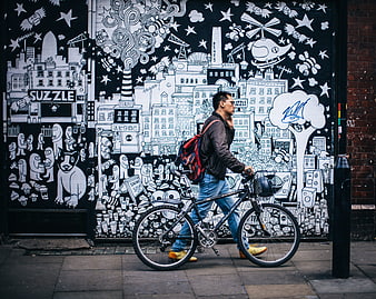 Man walking bicycle past black and white street art mural