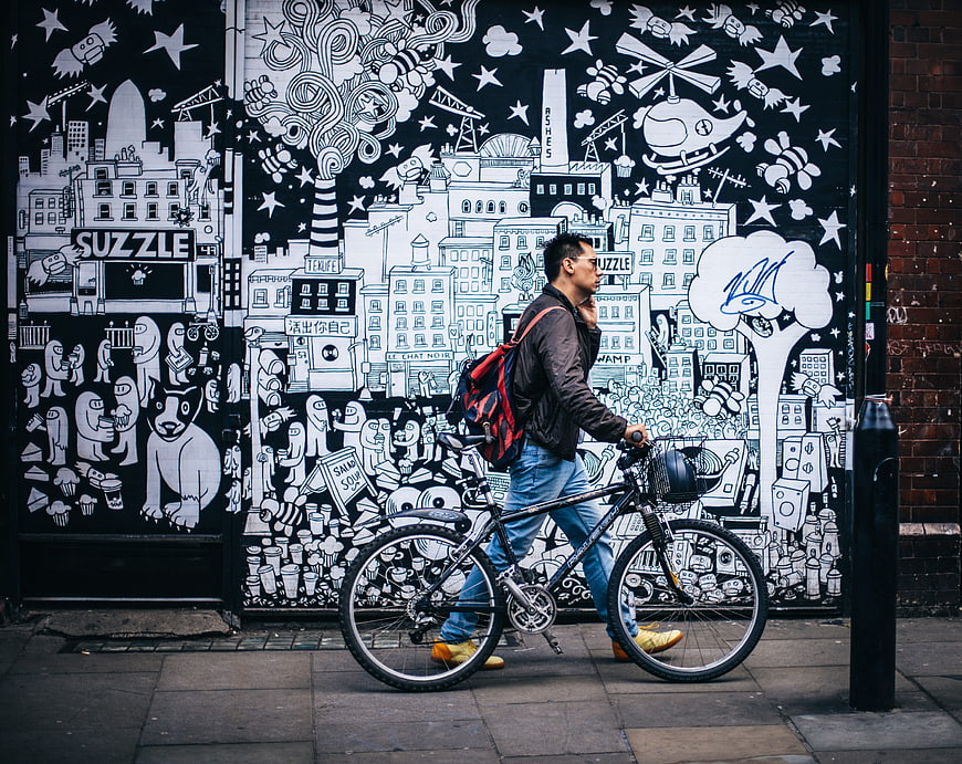 Man walking bicycle past black and white street art mural