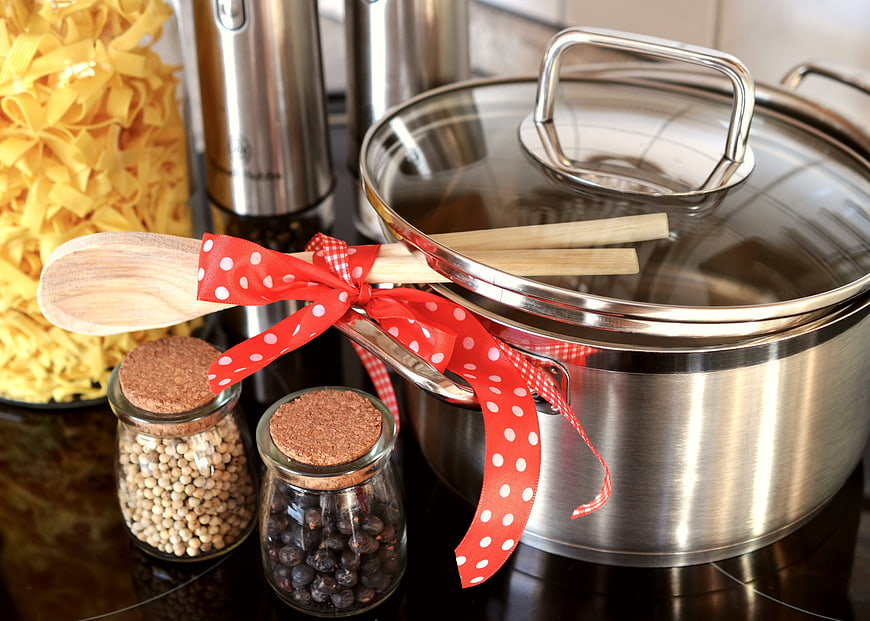 Stainless steel pot with wooden spoon and red ribbon on kitchen counter