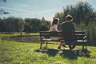 Couple Sitting on Park Bench by Pond in Sunlight