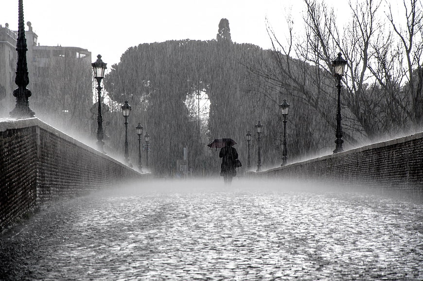 Lonely figure with umbrella walking on a rainy bridge in Paris