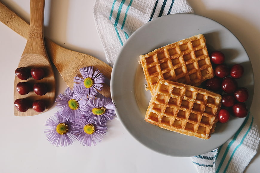 Overhead view of waffles and cherries with purple flowers