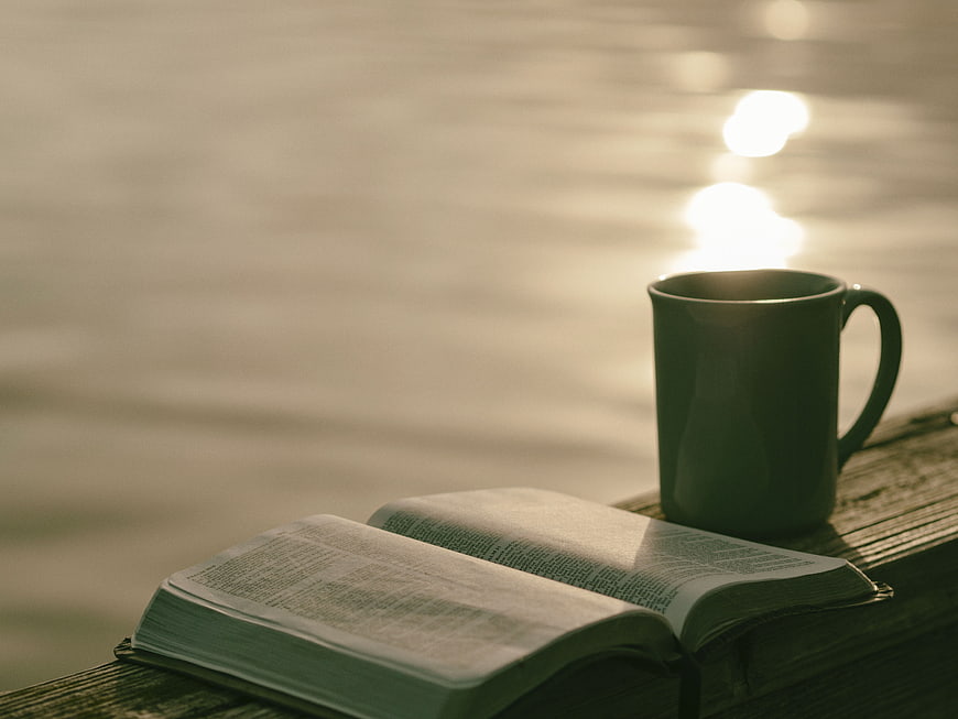 Open book and coffee mug on wooden dock by water