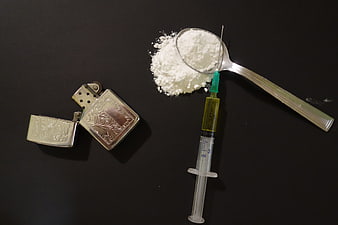 Syringe, spoon, and lighter with white powder on black background