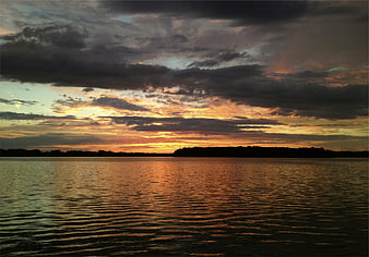 Dramatic sunset over a calm lake with dark clouds