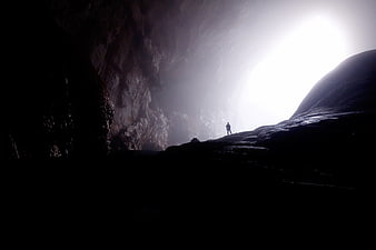 Silhouette of Explorer Standing in Dark Cave Entrance