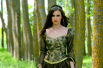 Young woman in medieval dress and tiara standing in a green forest