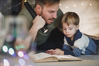 Father and son reading book with flashlight indoors