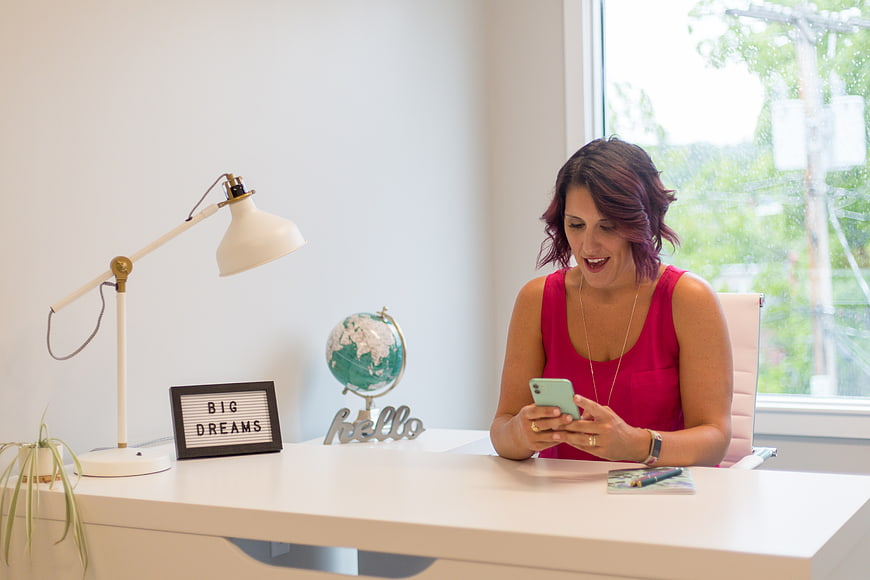 Woman smiling at smartphone in bright home office workspace
