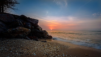 Sunset over rocky pebble beach with ocean waves
