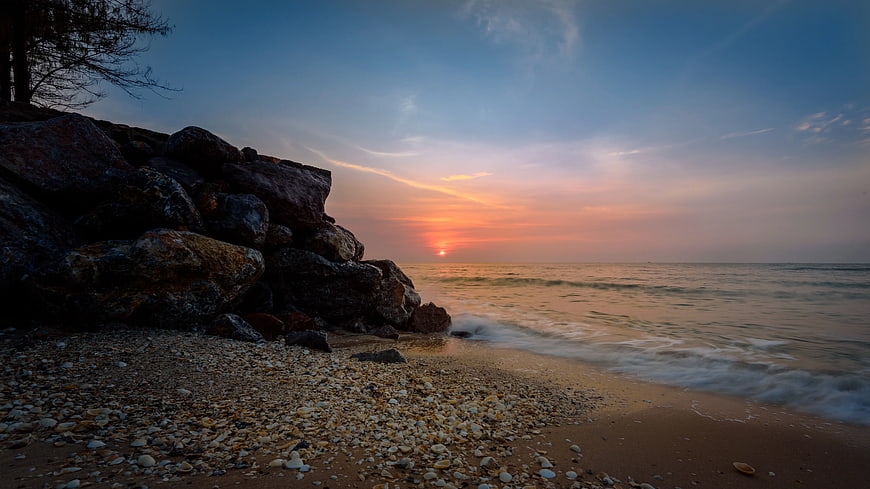 Sunset over rocky pebble beach with ocean waves