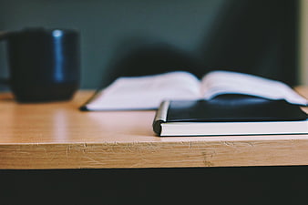 Black Notebook and Open Book on Wooden Desk