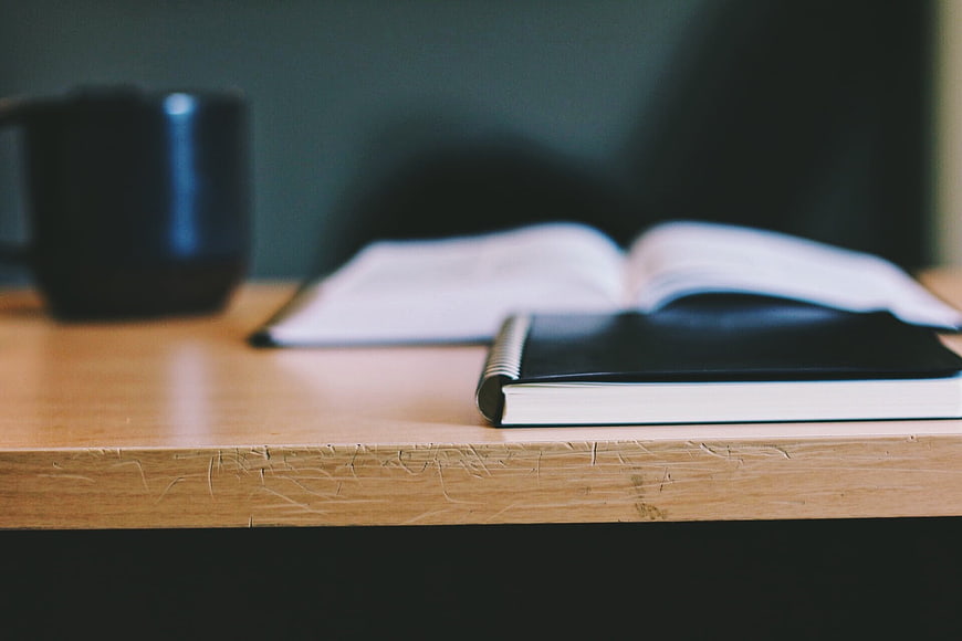 Black Notebook and Open Book on Wooden Desk
