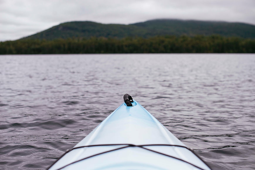Blue Kayak Bow on Calm Lake with Mountain Background