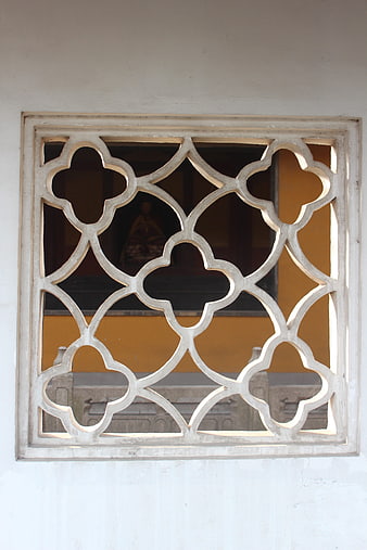 Ornate white quatrefoil window lattice with yellow wall background