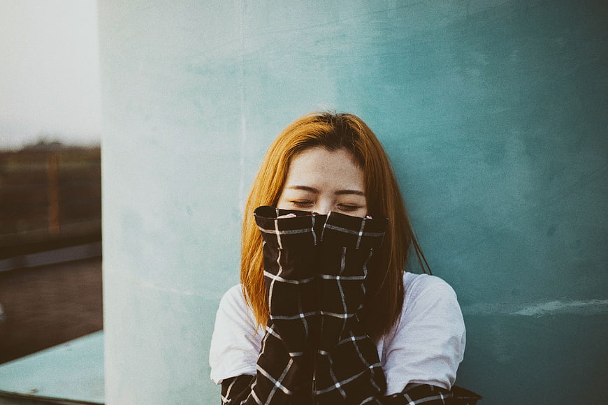 Young woman with eyes closed covering face with plaid sleeve