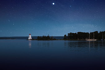 Lighthouse and Starry Night Sky Over Calm Water