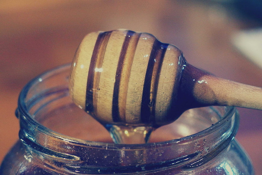 Close-up of wooden honey dipper dripping honey from glass jar