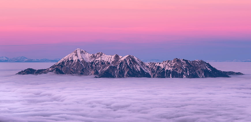 Snowy Mountain Peak Rising Above Sea of Clouds at Pink Sunset