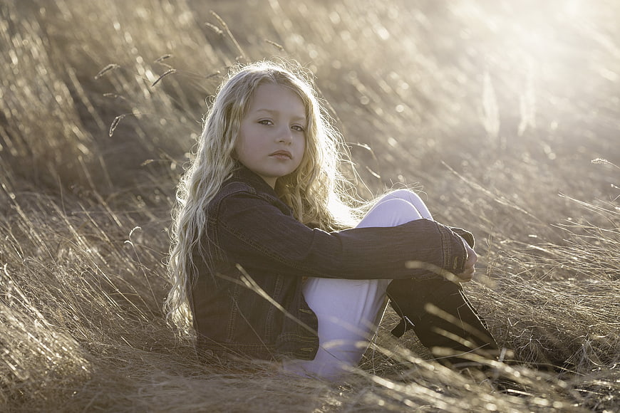 Young Girl Sitting in Golden Field at Sunset