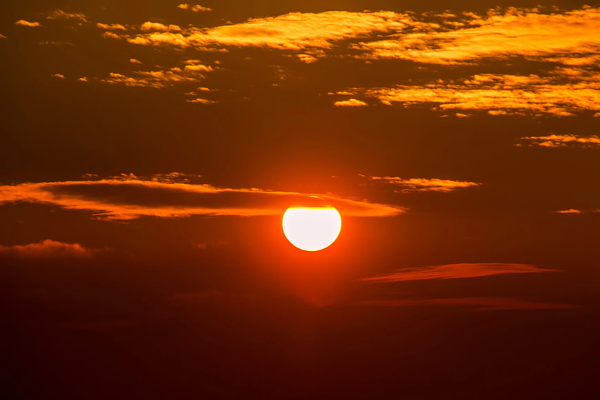Vibrant orange sunset with bright sun and scattered clouds